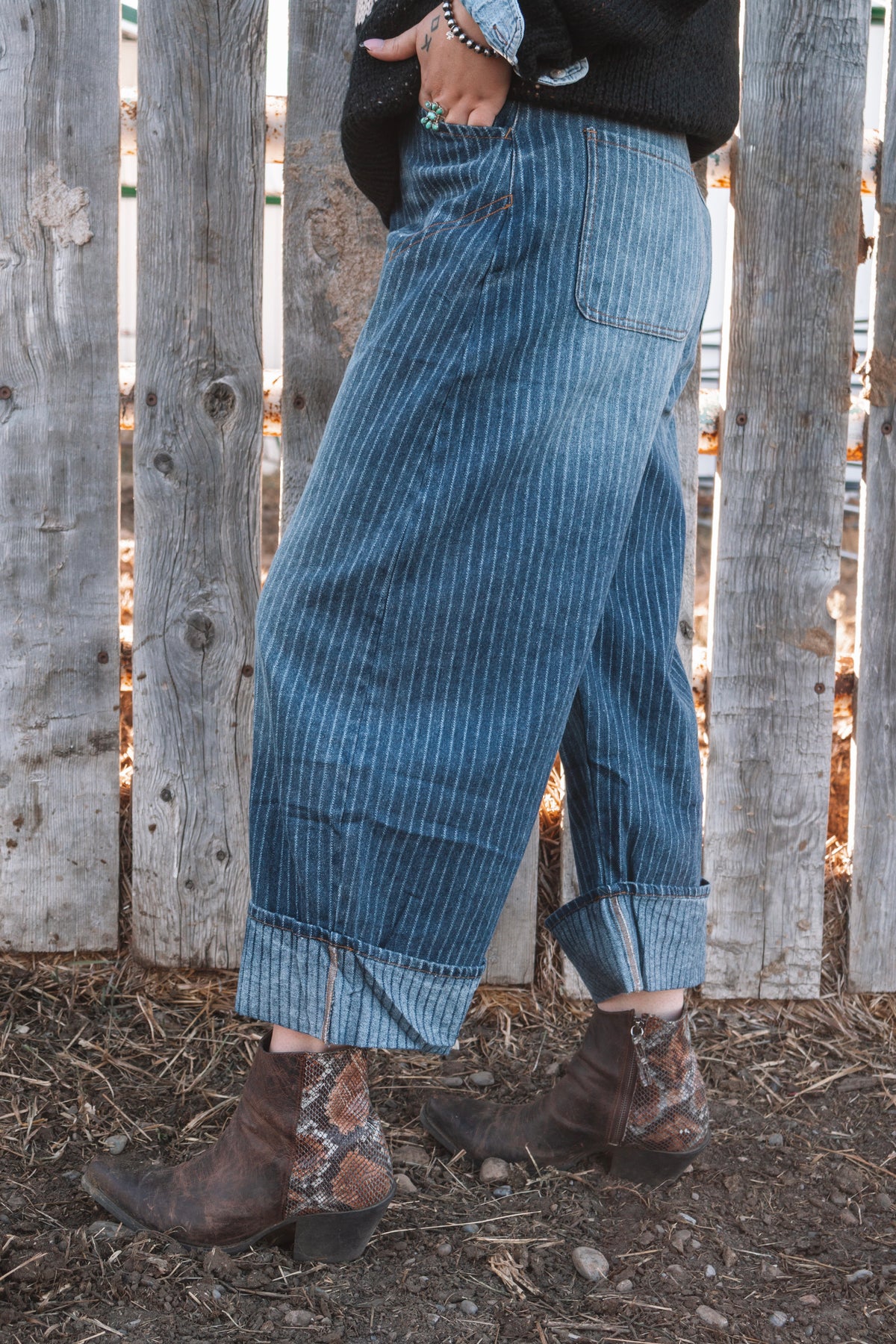 Side view of women's blue pinstripe wide leg denim jeans showing the relaxed fit, oversized folded cuffs, back pocket and brown ankle boots.