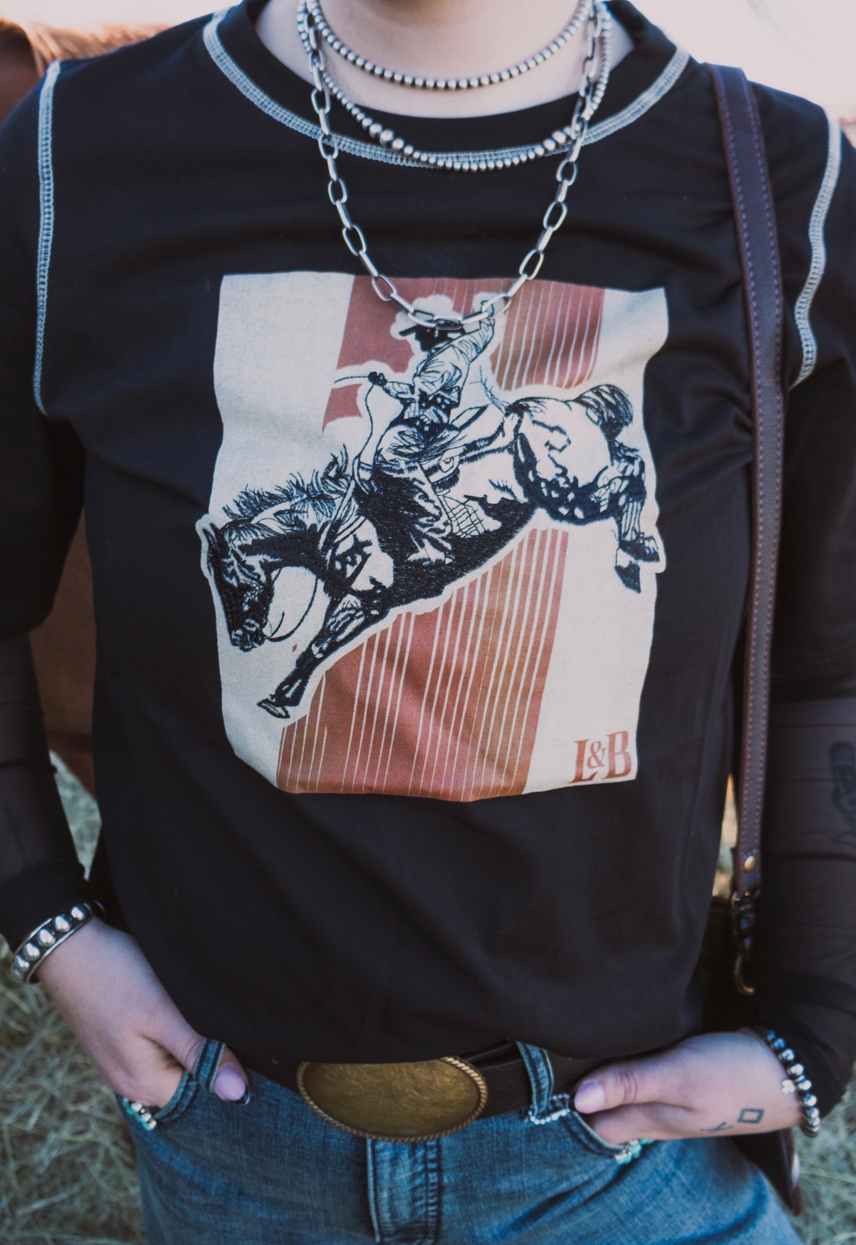 Close-up of black western graphic tee featuring a bronc rider design with rust-coloured stripes and a cream background