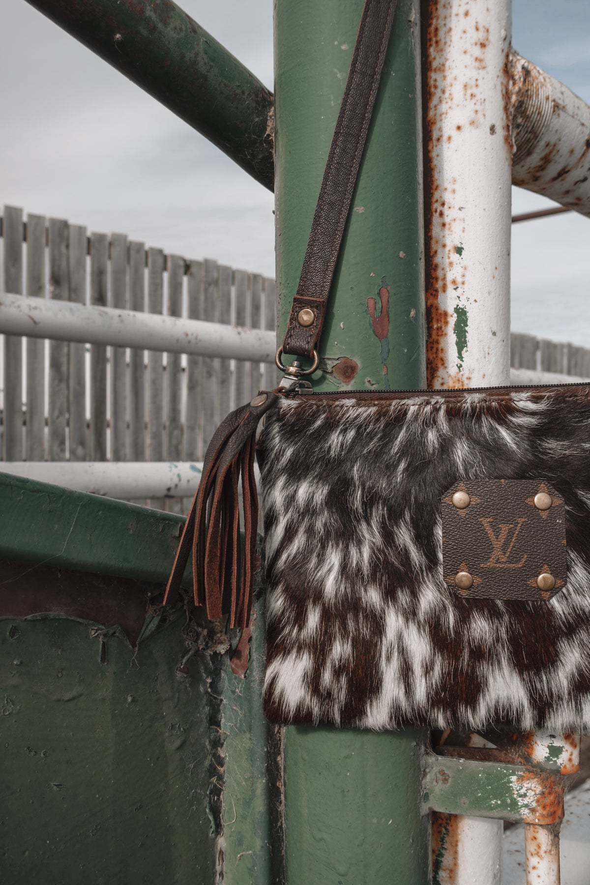 Close-up of cowhide crossbody purse showing brown leather tassel, detachable shoulder strap, and zippered closure.