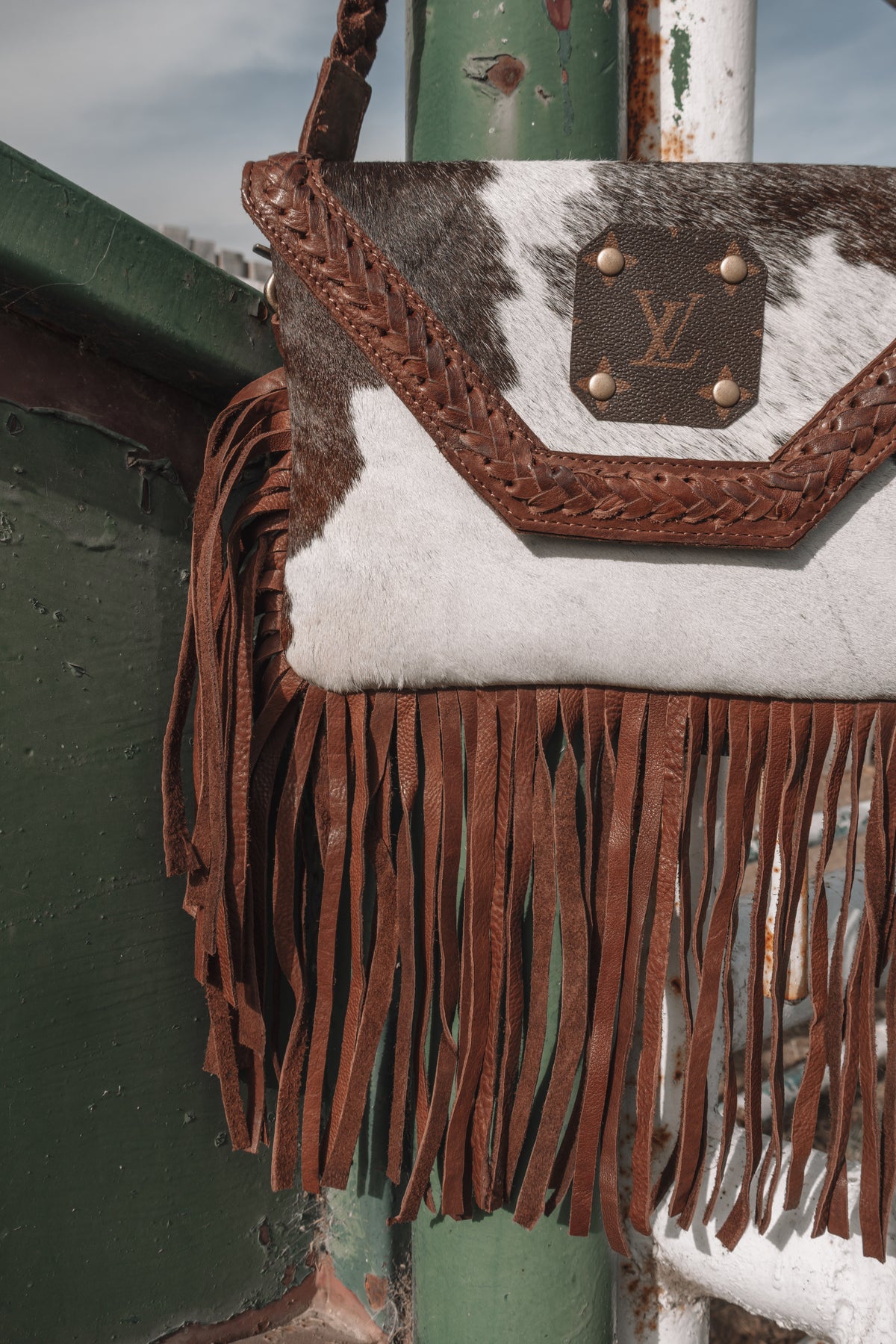 Close-up of genuine cowhide western bag featuring brown braided leather trim, LV monogram patch, and long leather fringe.