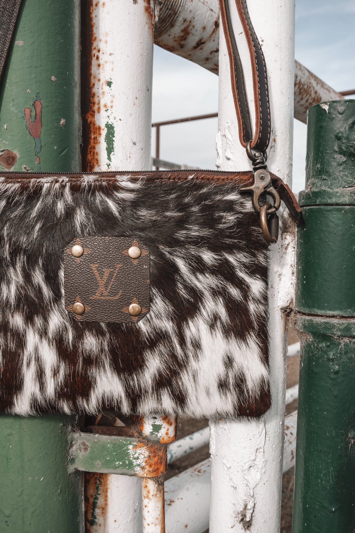 Close-up of brown and white cowhide crossbody bag with LV monogram patch, brass-tone hardware, and dark brown leather strap