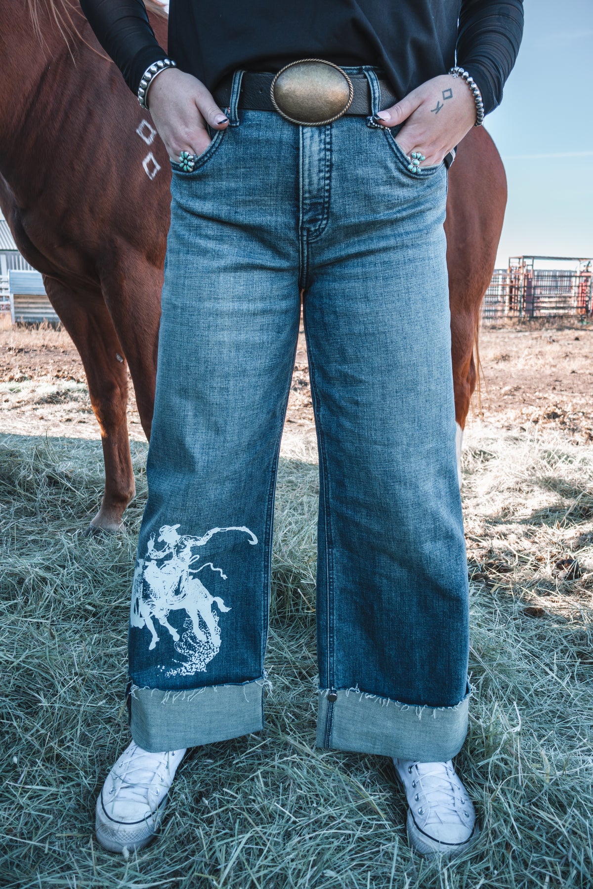 Women's high rise western wide leg jeans in medium stonewash denim, featuring a white bronc rider graphic, tummy control fit, and adjustable rolled cuffs.
