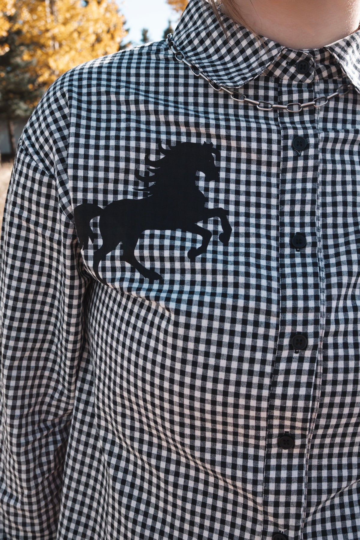 Close-up of black horse silhouette graphic on a black and white gingham button down shirt with pointed collar and black buttons.