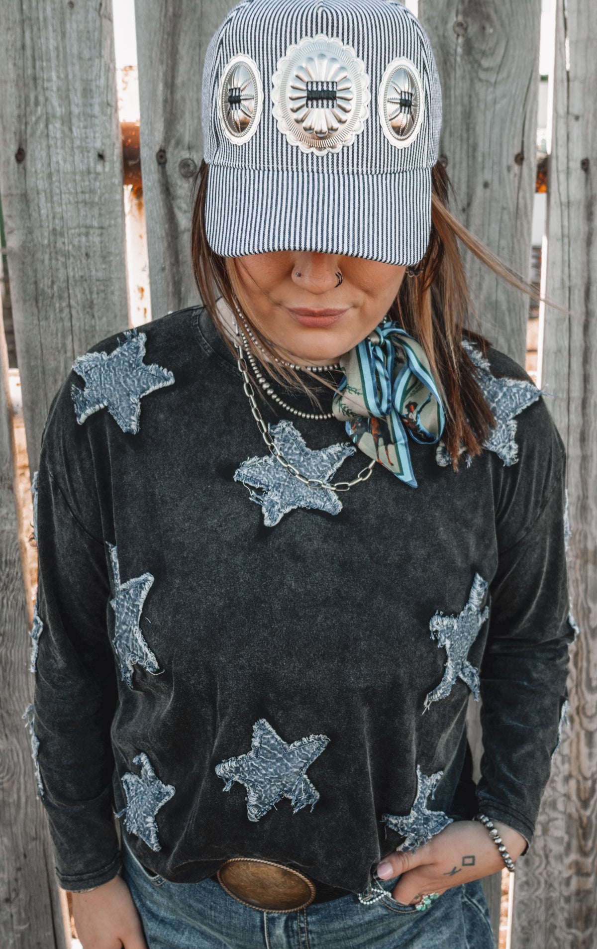 Women's washed black denim star patch long sleeve top featuring textured blue denim stars across the chest, shoulders and sleeves, styled with a pinstripe western baseball cap and turquoise twilly.