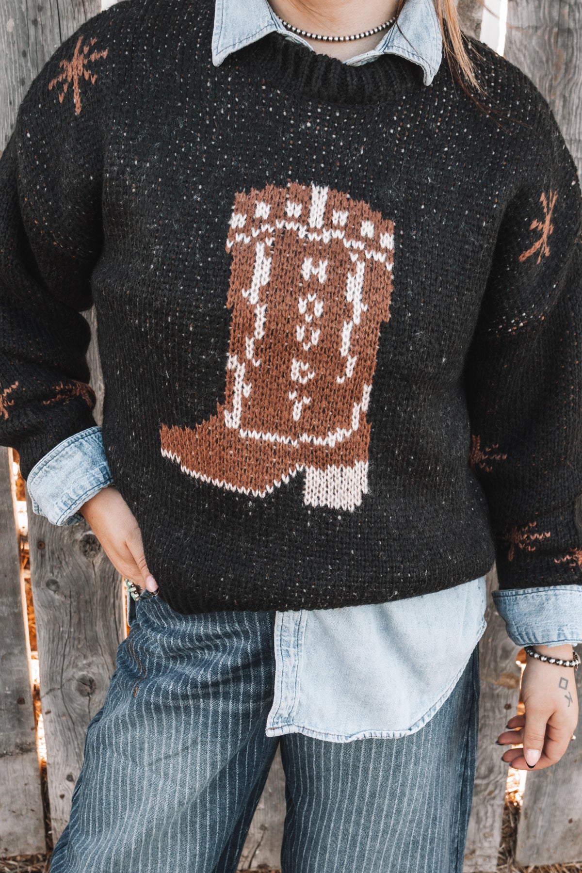Close-up of women's black western knit sweater featuring a brown cowboy boot design with white detailing on the front.