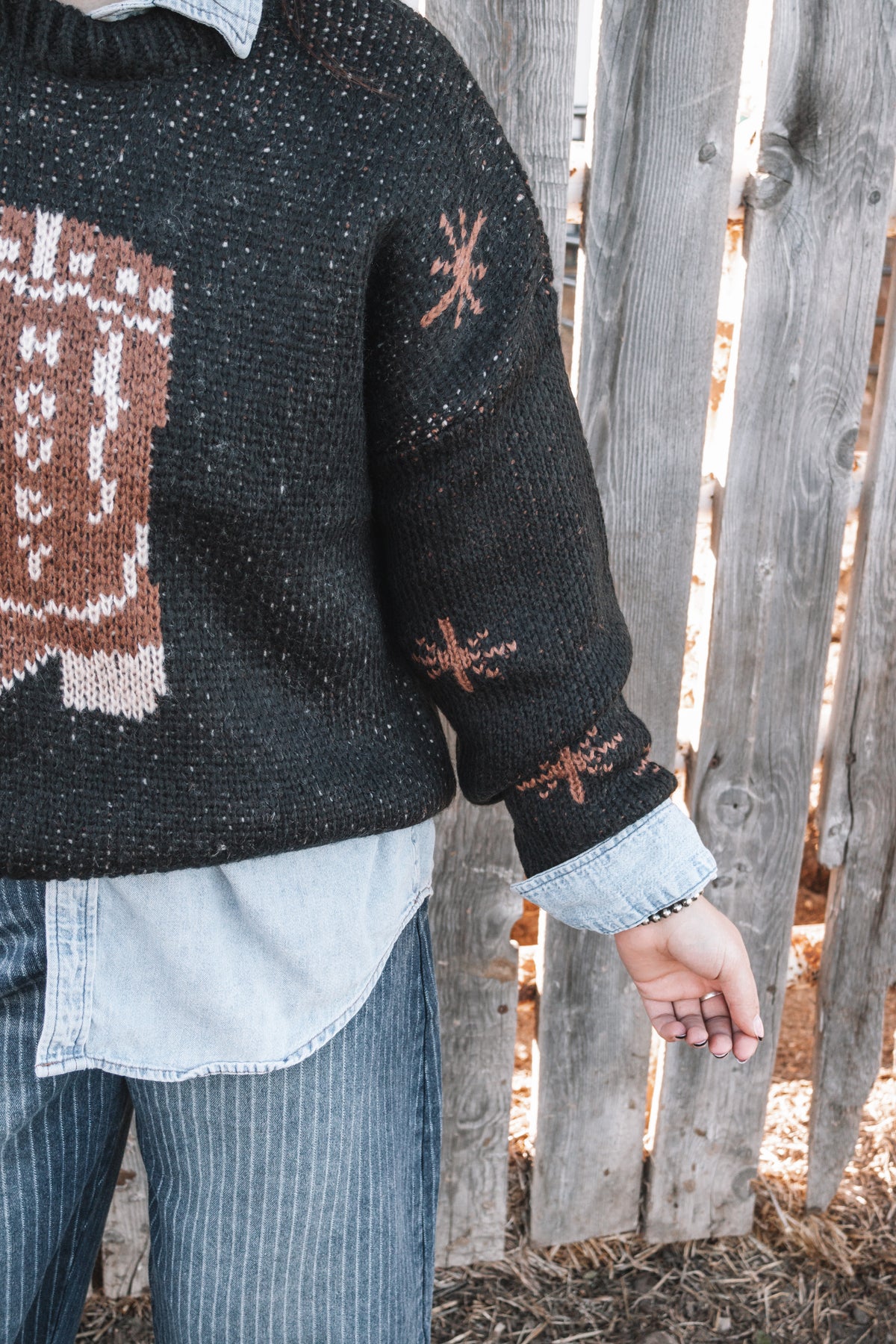 Close-up of black cowboy boot graphic sweater showing textured knit fabric, brown western detailing, and ribbed trim.