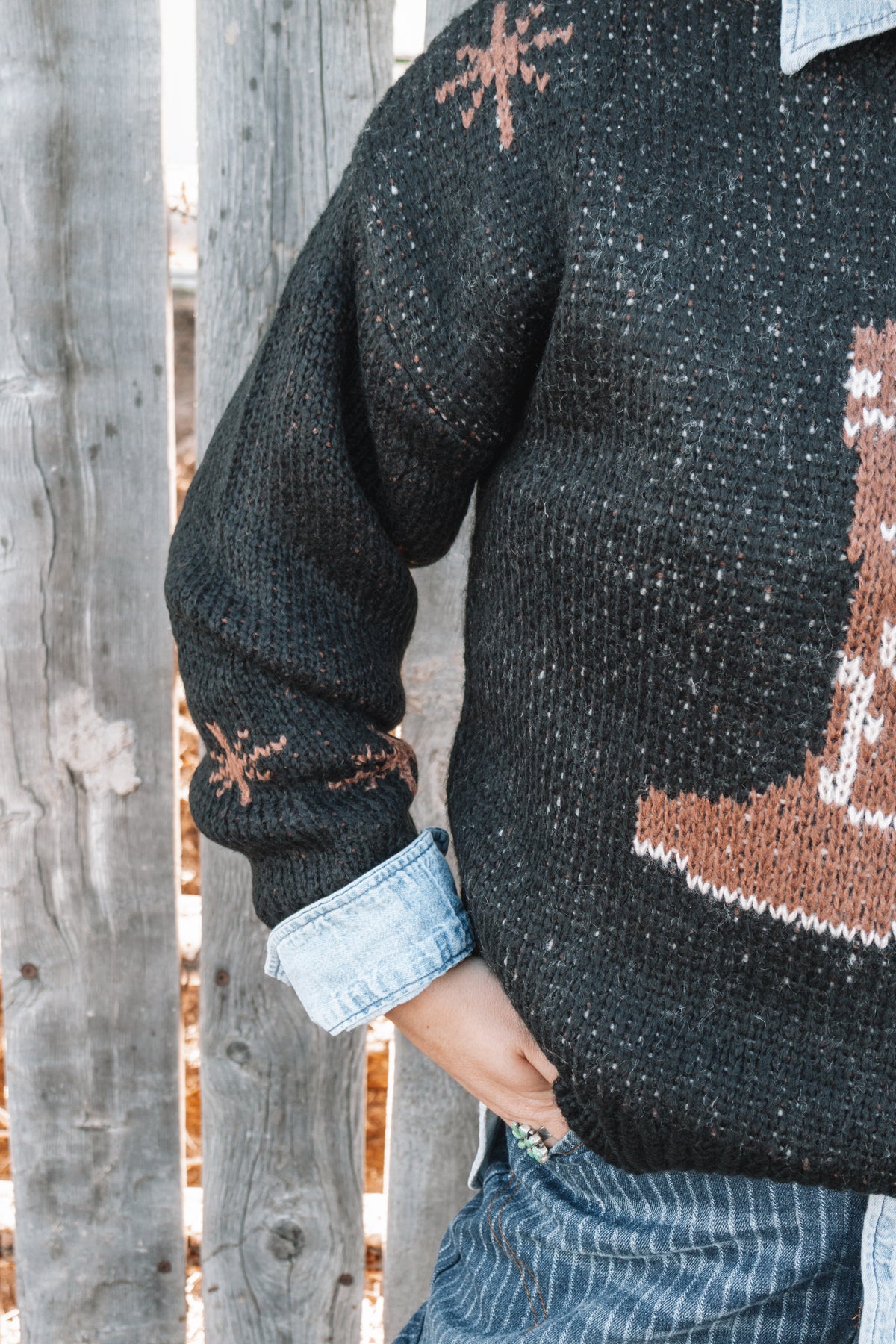 Black western knit sweater featuring subtle brown western-inspired patterns on the long sleeves and ribbed knit cuffs.
