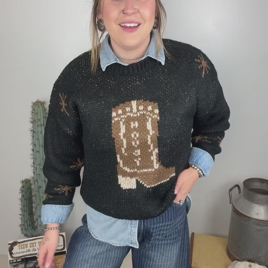 Women's black western cowboy boot knit sweater styled over a light wash denim button down with striped wide leg jeans and brown ankle boots.