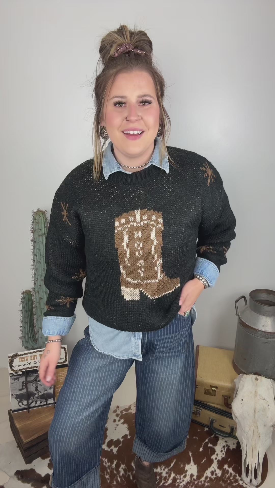 Women's black western cowboy boot knit sweater styled over a light wash denim button down with striped wide leg jeans and brown ankle boots.